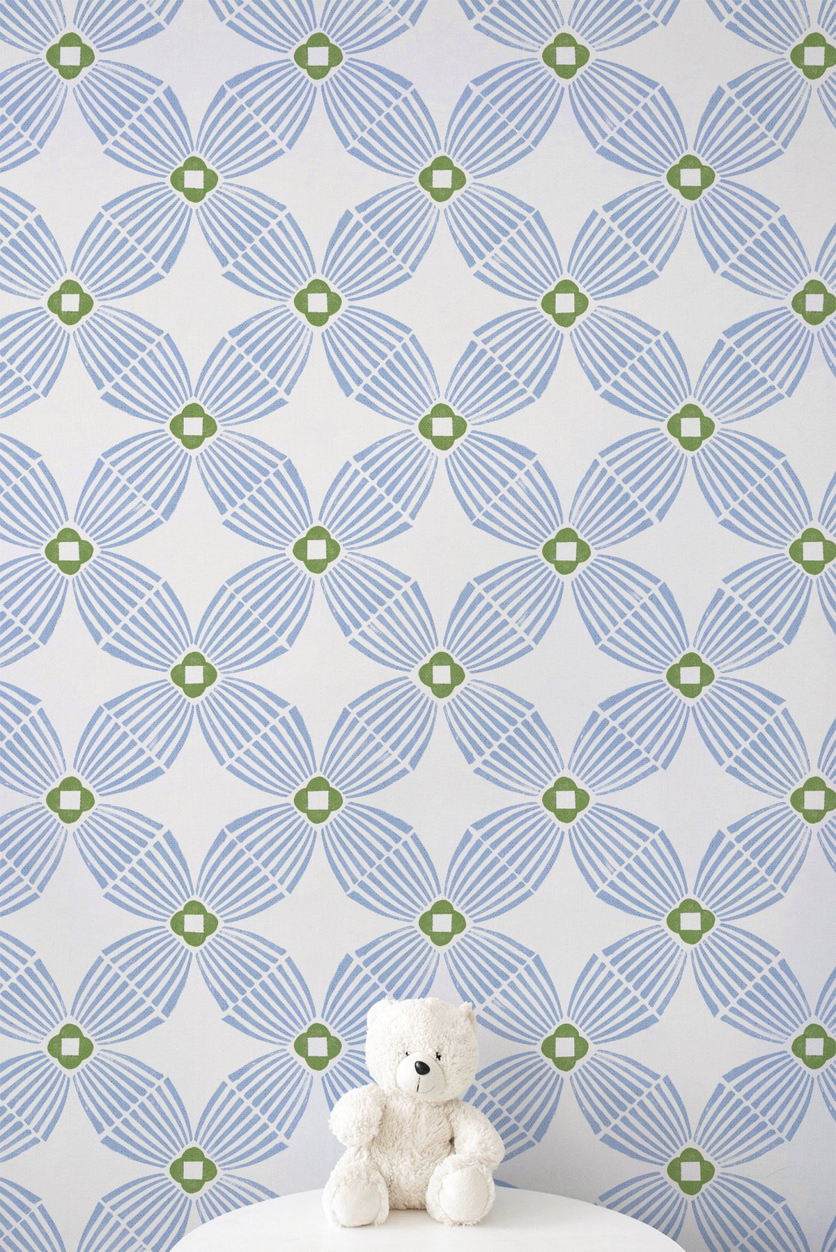 Blue and green geometric patterned wallpaper with a small white teddy bear sitting on a white surface at the bottom.