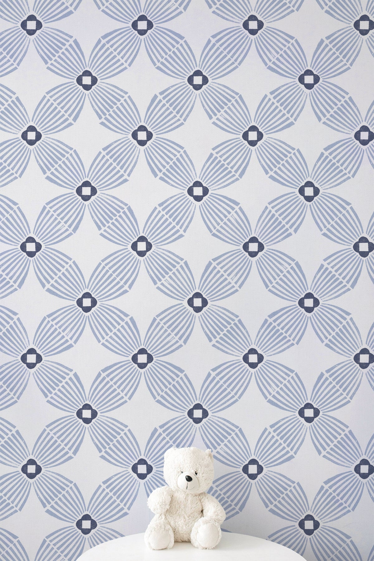 Blue and white geometric patterned wallpaper with a small white teddy bear sitting on a white surface at the bottom.