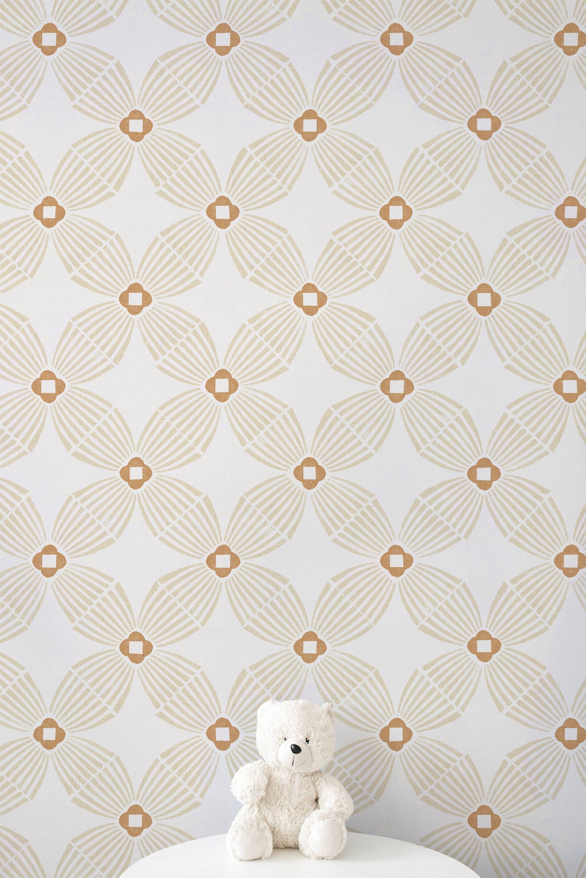 A white teddy bear sits on a white pedestal against a wall covered in repeating geometric wallpaper with a warm beige and white pattern.