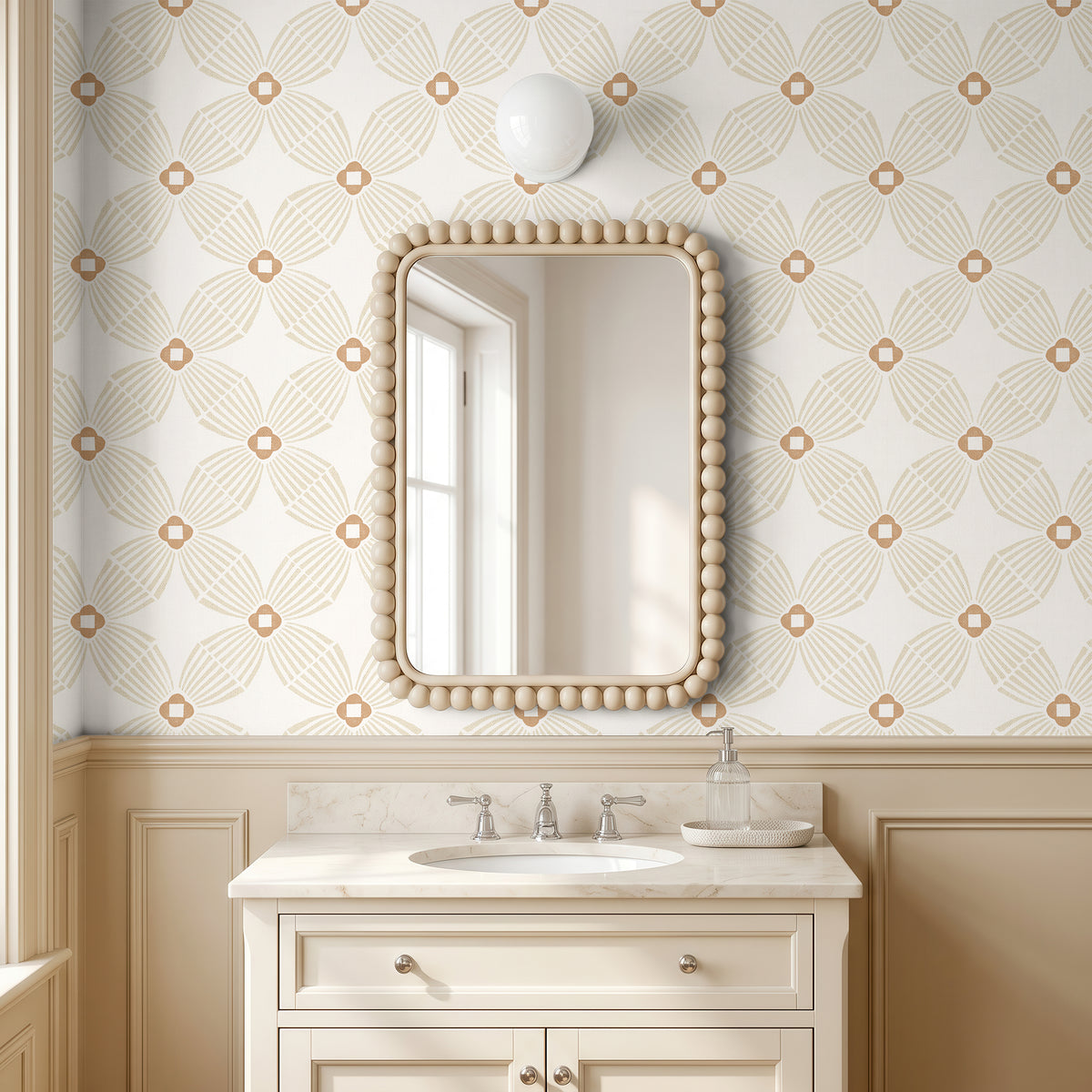 A bathroom vanity scene with a rectangular mirror featuring a beaded frame, mounted on geometric wallpaper in muted tan and beige above a white sink cabinet and a tan wainscoted wall.