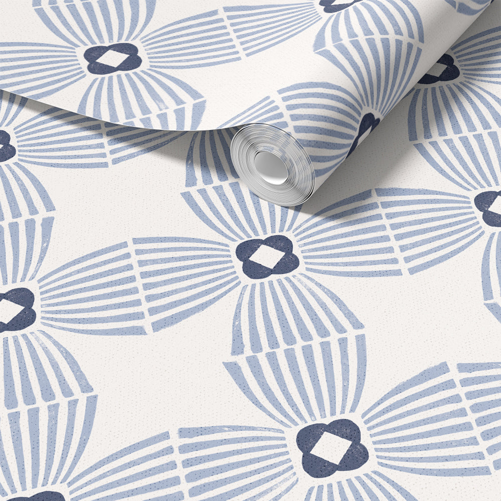 A roll of wallpaper with a repeating geometric fan and diamond pattern in light blue and dark navy on a white background, partially unrolled to show the surface.
