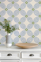 Blue and green geometric patterned wallpaper styled on a wall above a white wooden dresser with a vase of eucalyptus and a wooden bowl.