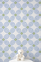 Blue and green geometric patterned wallpaper with a small white teddy bear sitting on a white surface at the bottom.