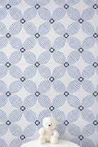 Blue and white geometric patterned wallpaper with a small white teddy bear sitting on a white surface at the bottom.
