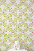 A white wall covered in a repeating geometric wallpaper pattern with lime green and pink floral motifs, with a small white teddy bear sitting on a white surface at the bottom.