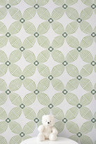 Green and white geometric patterned wallpaper with a small white teddy bear sitting on a white surface at the bottom.