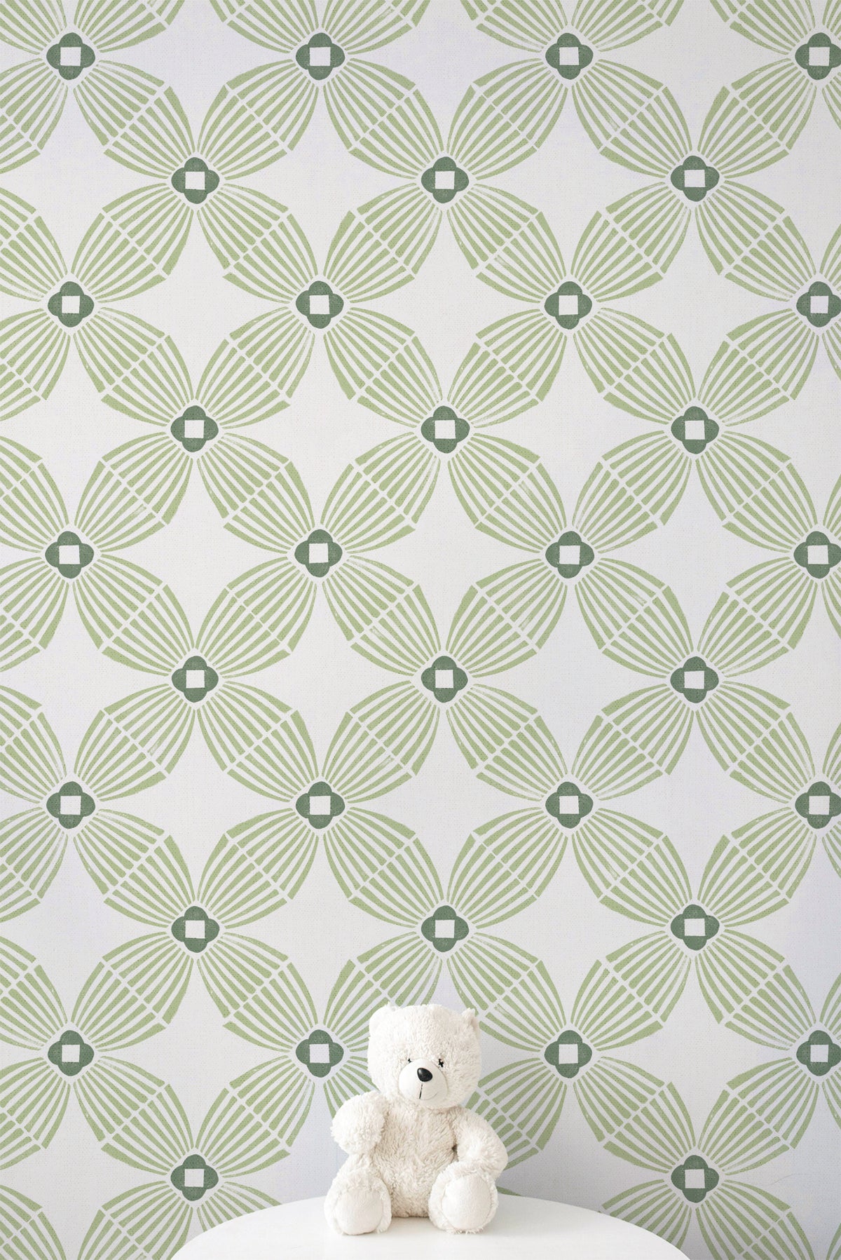 Green and white geometric patterned wallpaper with a small white teddy bear sitting on a white surface at the bottom.