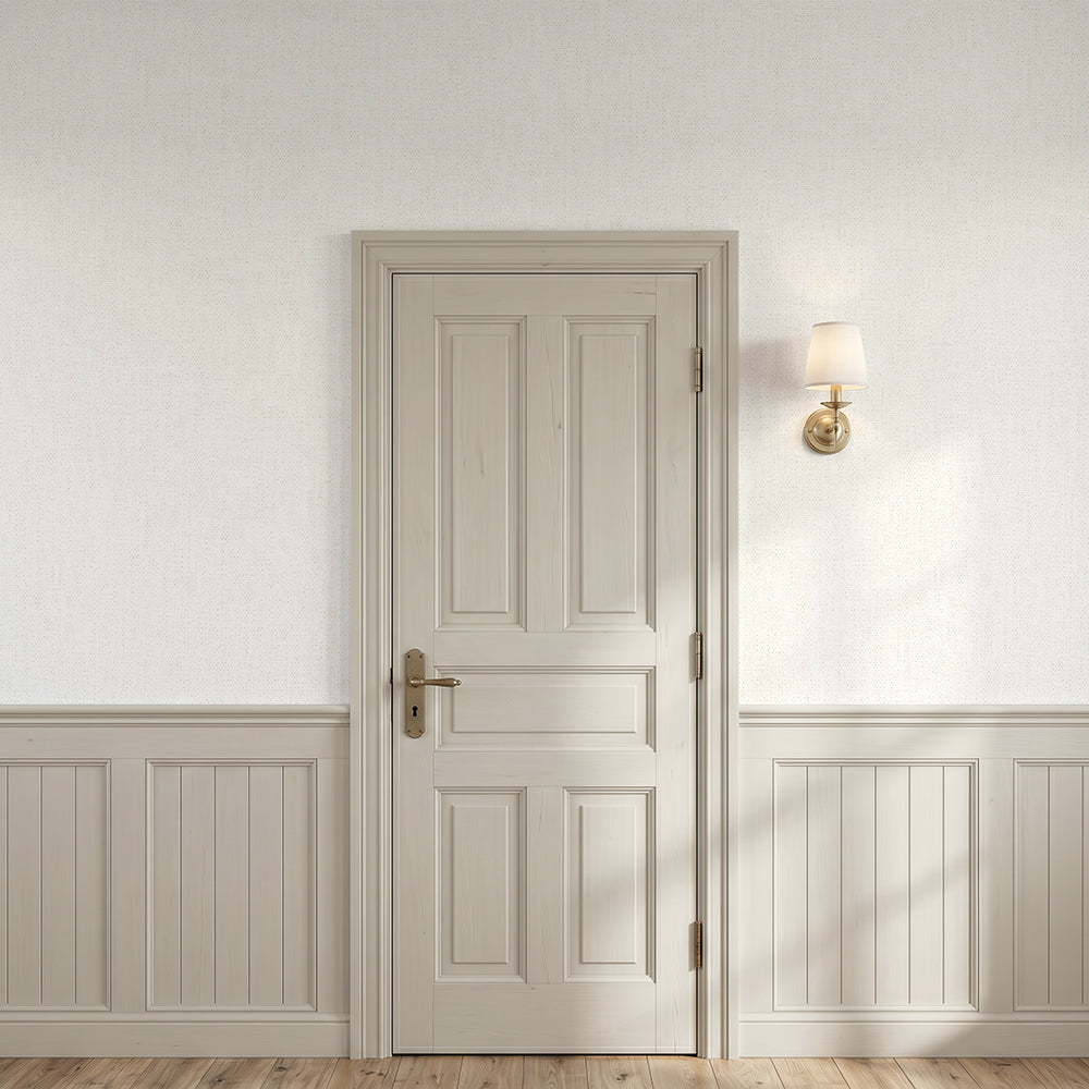 A classic six-panel interior door in a warm beige/cream finish, set within a matching door frame on a wall with paperhaze wallpaper in warm beige with white wainscoting and a gold wall sconce.