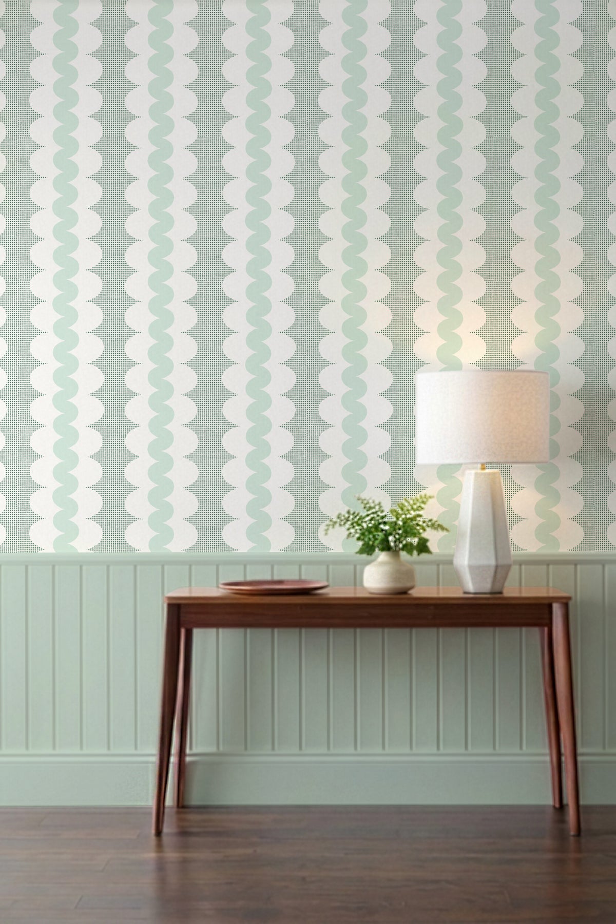 A styled interior scene showing a wall with vertical wavy stripes in pale mint green and white, above a wooden console table with a lamp and small plant.