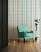 A modern mint green armchair with black legs sits in a styled room with a patterned grandmilennial striped wallpaper background, a brass floor lamp, and a small side table with a vase.
