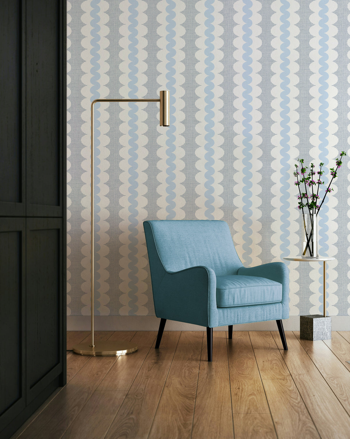 A styled interior scene featuring a light blue upholstered armchair in front of patterned wallpaper, with a gold floor lamp and a small side table holding a vase with branches.