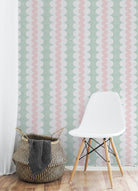 A styled interior corner showing a pale mint green wallpaper with vertical wavy stripes in white and soft pink, a white molded side chair with wooden legs, a woven basket, and a light wood floor.