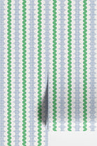 Light blue and white patterned wallpaper with vertical green wavy stripes, shown partially unrolled with a fold revealing a white surface underneath.