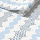 A roll of wallpaper with a repeating pattern of light blue wavy stripes, white cloud-like shapes, and dark blue square dots on a white background.