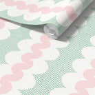 A roll of wallpaper with a retro pattern of pink wavy lines, green square dots and white oval shapes, shown partially unrolled on a white surface.