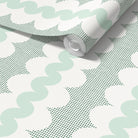 A roll of wallpaper with a retro pattern, partially unrolled to show the design. The pattern features mint green wavy lines and green square dots on a white background.
