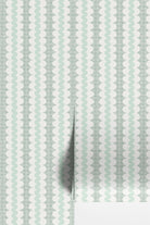 A close-up of wallpaper with a repeating vertical pattern of pale mint green and white wavy scallop shapes over a subtle light gray grid, with a folded corner showing a white surface underneath.