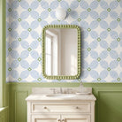 A bathroom vanity scene with a rectangular mirror featuring a green beaded frame, mounted on a wall with blue and green floral wallpaper. Below the mirror is a white marble countertop, white sink, and a white cabinet with silver knobs.