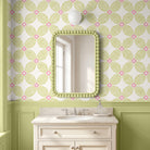A bathroom vanity featuring a rectangular mirror with a green beaded frame, set against wallpaper with a green and pink geometric pattern and a bright lime green  wainscoted wall.