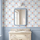 A bathroom vanity scene with a cream-colored sink cabinet, a light blue beaded mirror frame, and wallpaper featuring a repeating blue and orange floral pattern above a light blue wainscoted wall.