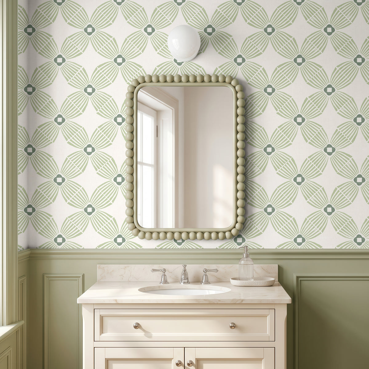 A bathroom vanity scene with a rectangular mirror featuring a beaded frame, mounted on wallpaper with a green and white geometric pattern. Below the mirror is a white pedestal sink with a marble countertop and chrome faucet.