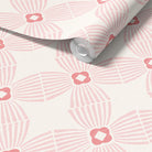 A roll of wallpaper with a repeating pink and white geometric fan pattern, partially unrolled to show the texture and design.
