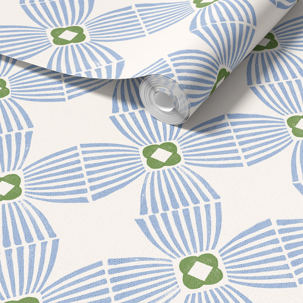 A roll of wallpaper with a repeating geometric pattern in light blue and olive green on a warm off-white background, shown partially unrolled.