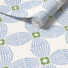 A roll of wallpaper with a repeating geometric pattern in light blue and olive green on a warm off-white background, shown partially unrolled.