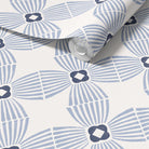A roll of wallpaper with a repeating geometric fan and diamond pattern in light blue and dark navy on a white background, partially unrolled to show the surface.