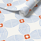 A roll of wallpaper with a repeating mid-century modern pattern featuring light blue striped fan shapes and orange flower-like centers on an off-white background.