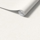 A roll of light beige wallpaper with a subtle paper textured pattern, shown partially unrolled over a matching flat surface.