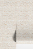 A close-up of a textured wallpaper or wall covering in a warm off-white/cream tone with subtle horizontal beige striations, shown with a folded corner casting a soft shadow.