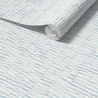 A roll of light beige wallpaper with a subtle horizontal woodgrain pattern, shown partially unrolled over a matching flat surface.