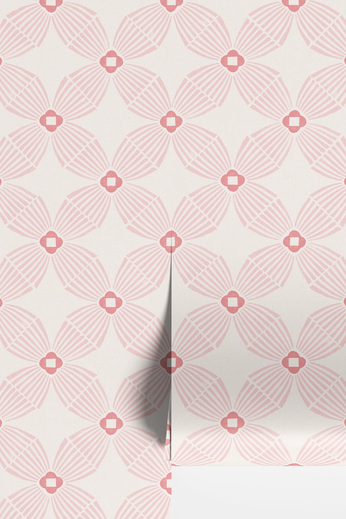 Pink and white geometric wallpaper rolls with a repeating fan-like pattern and small diamond medallions, shown with a folded corner revealing a white surface underneath.