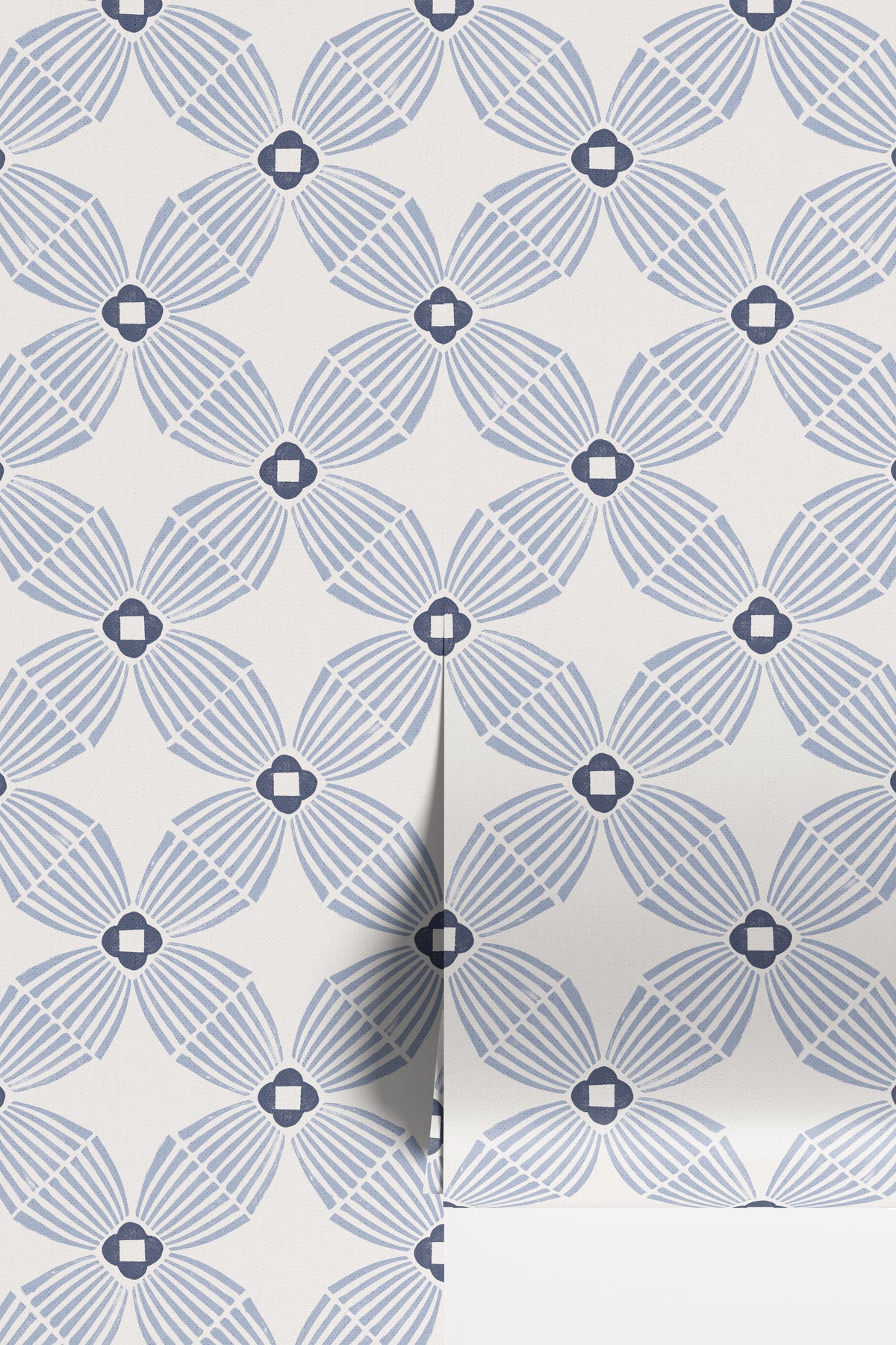 A close-up of wallpaper with a repeating geometric floral pattern in muted blue-gray on an off-white background, with a folded corner showing the texture and layering.