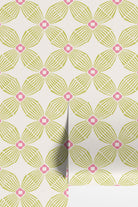 A close-up of wallpaper rolls with a repeating geometric floral pattern in light lime green and hot pink on an off-white background.